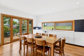 A modern kitchen with a dining area, large windows, and a view of the outdoors.