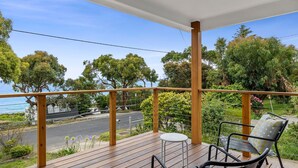 A wooden deck with a table and chairs, overlooking a road and trees. - Smith (Lorne)