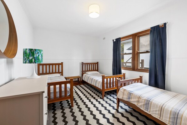 A room with two wooden beds, a desk, a mirror, and a window with curtains.