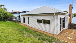 A single-story house with a sloped roof, a fenced backyard, and a view of the water. - Smith (Lorne)