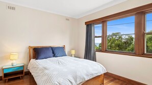 A bedroom with a wooden bed, two bedside tables with lamps, a window with curtains, and a view of greenery outside. - Smith (Lorne)