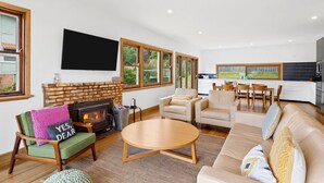 A modern living room with a fireplace, a flat-screen TV, and a dining area with a kitchen in the background. - Smith (Lorne)