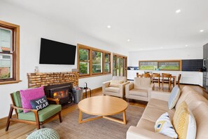 A modern living room with a fireplace, a flat-screen TV, and a dining area with a kitchen in the background. - Smith (Lorne)
