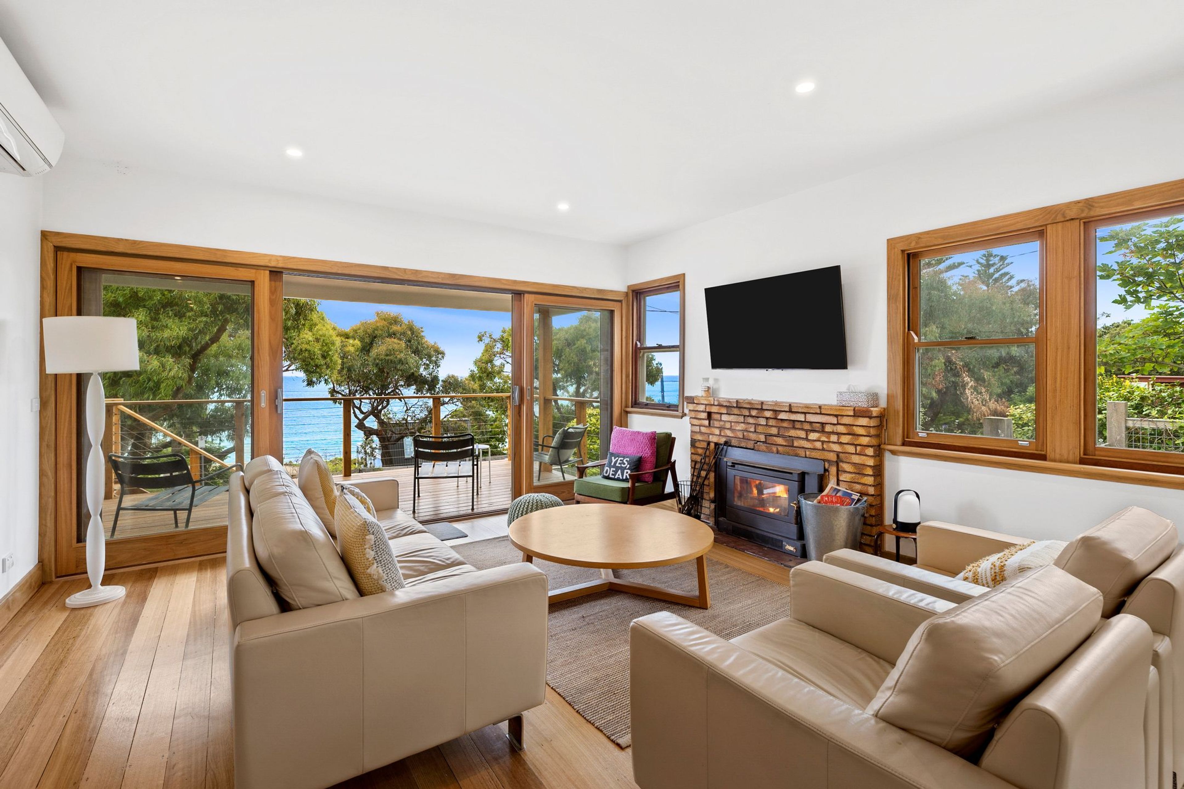 A spacious living room with a fireplace, comfortable seating, and large windows offering a view of the outdoors.