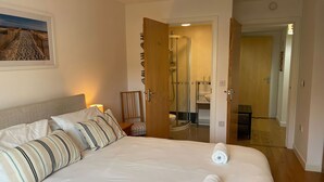 A neatly made bed with striped pillows, a glass-enclosed shower, and a wooden door leading to a bathroom.