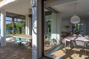 Ein moderner Essbereich im Freien mit einer Glastür, die auf eine Terrasse, einen Pool und die Außenlandschaft führt.