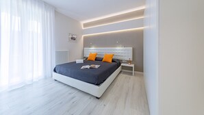 A modern bedroom with a large bed, white nightstands, and a bedside table with a lamp. - Appartamento Valeria by Wonderful Italy (Sirmione)