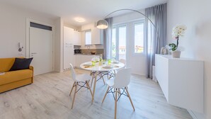 A modern kitchen with white cabinets, a dining table with chairs, and a yellow sofa. - Appartamento Valeria by Wonderful Italy (Sirmione)