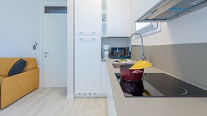 A compact kitchen with white cabinets, a microwave, a coffee maker, and a red pot on an induction cooktop. - Appartamento Valeria by Wonderful Italy (Sirmione)