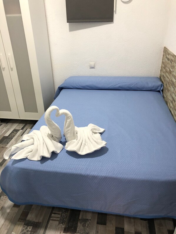 Un lit avec un matelas bleu et un téléviseur blanc fixé au mur.