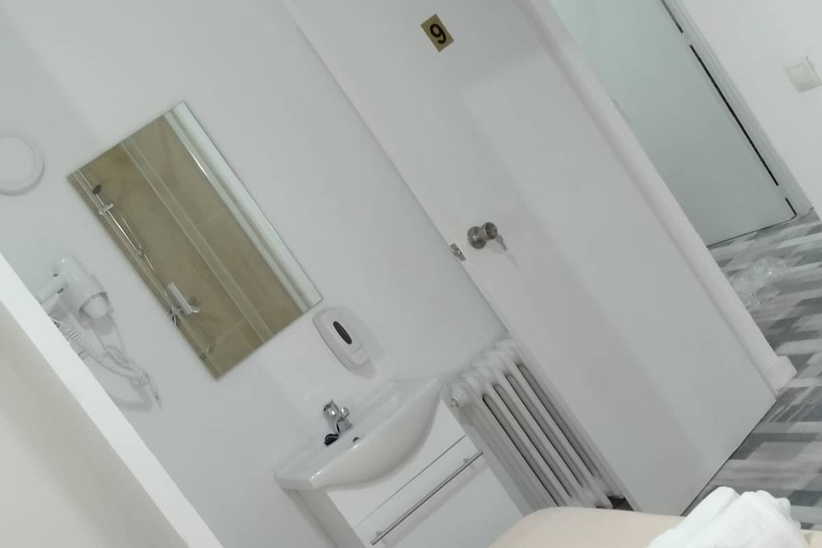 Habitación de hotel con cama, lavamanos, espejo y puerta que da a otra habitación.