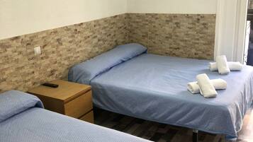 Una habitación con dos camas, cada una con cubrecama y almohadas azules, y una mesita de noche de madera con un control remoto.
