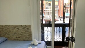 Habitación de hotel con cama, una silla y vista a la calle por una puerta abierta.
