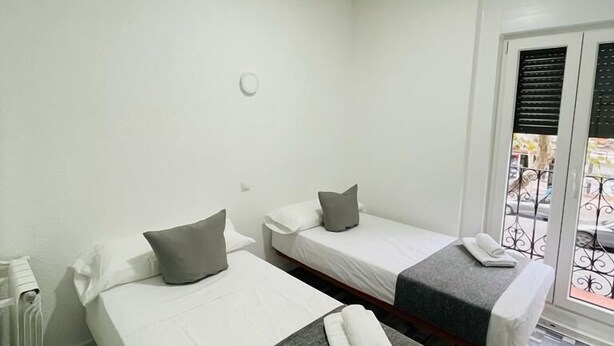Habitación de hotel con dos camas, un radiador, una ventana con persianas y vistas al exterior.