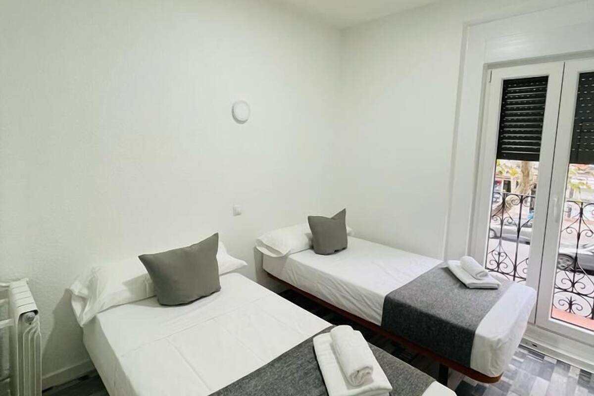 Habitación de hotel con dos camas, un radiador, una ventana con persianas y vistas al exterior.