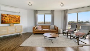 A spacious living room with a leather sofa, a round coffee table, and a view of the outdoors through large windows. - Bass River Farm 9 mins from Phillip Island (Bass)
