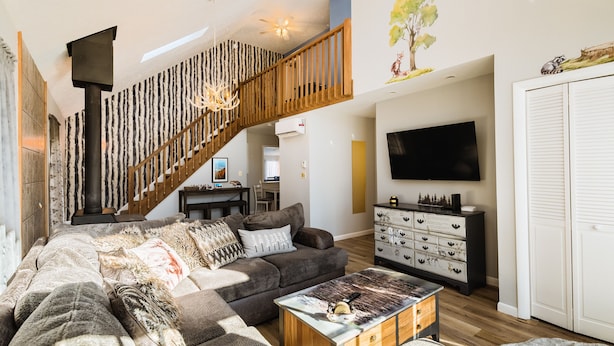 A modern living room with a staircase, a sofa, a coffee table, a TV, and a dresser. - BRAND NEW HOT TUB-SAUNA-2 WEBER GRILLS-FIRE PIT-AC-THERMOMIX (Long Pond)