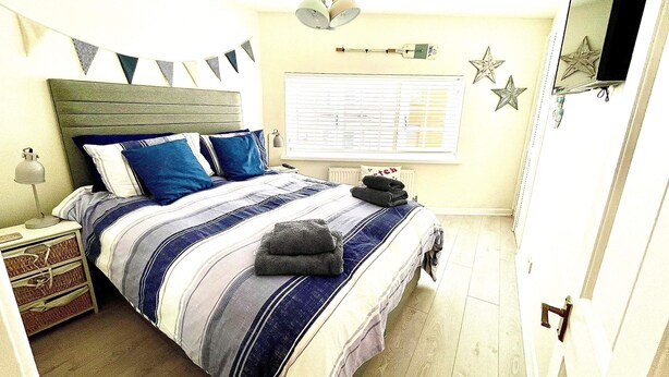 Quarto bem organizado com cama, mesa de cabeceira, abajur e janela com persianas.