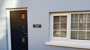 A door with a nameplate reading "Newton Cottage," a window with blinds, and a white trim around the window.