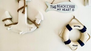 Decoração de parede com tema náutico, incluindo um círculo salva-vidas e uma placa com a inscrição 'The Beach is Where My Heart is'.
