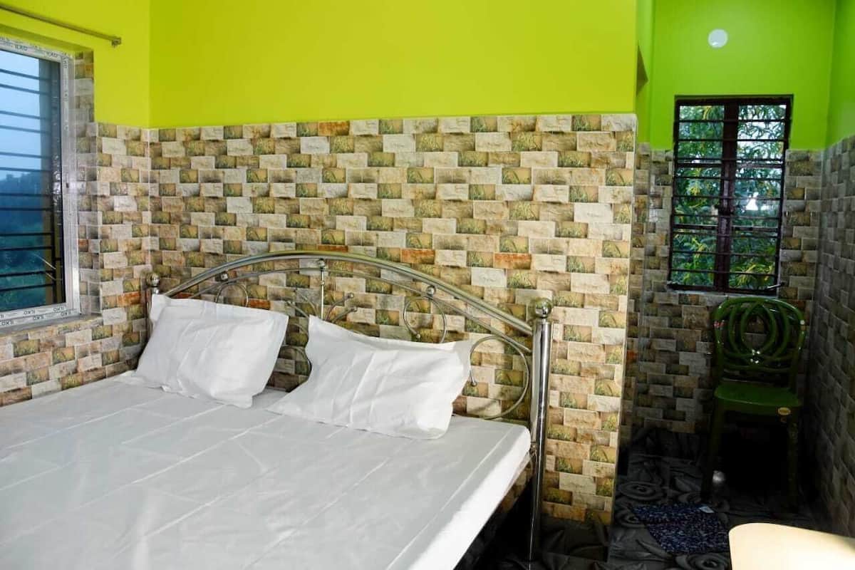 Ein Bett mit Metallgestell, ein Fenster mit Gitterstäben, eine grüne Wand und eine Wand mit Muster hinter dem Bett.