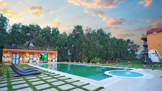 A swimming pool with a sun lounger and a mural, surrounded by greenery and a mural of a man. - Neel Nirjan Resort (Bolpur)