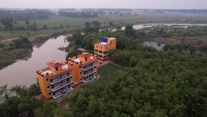 A multi-story building with balconies, surrounded by dense greenery and a body of water. - Neel Nirjan Resort (Bolpur)
