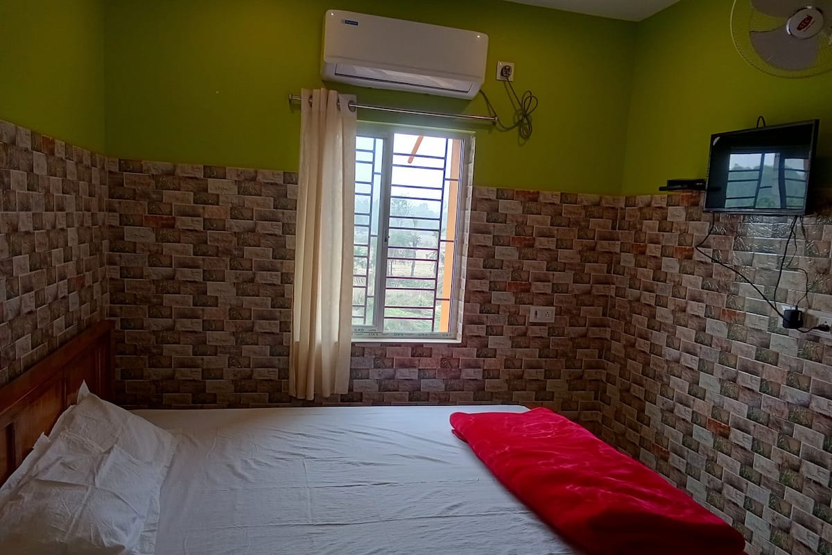 Ein Zimmer mit einem Bett, einem fensterbelaubten Fenster, einer ziegelartigen Wand und einer Klimaanlage.