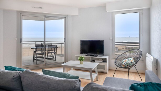 Een moderne woonkamer met balkon, een flatscreen televisie, een witte salontafel en een comfortabele zithoek.