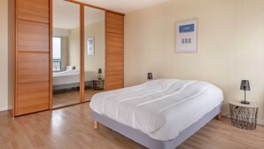 Een slaapkamer met een bed, een kledingkast, een rond bijzettafeltje, een lamp en een inlijsting diploma aan de muur.