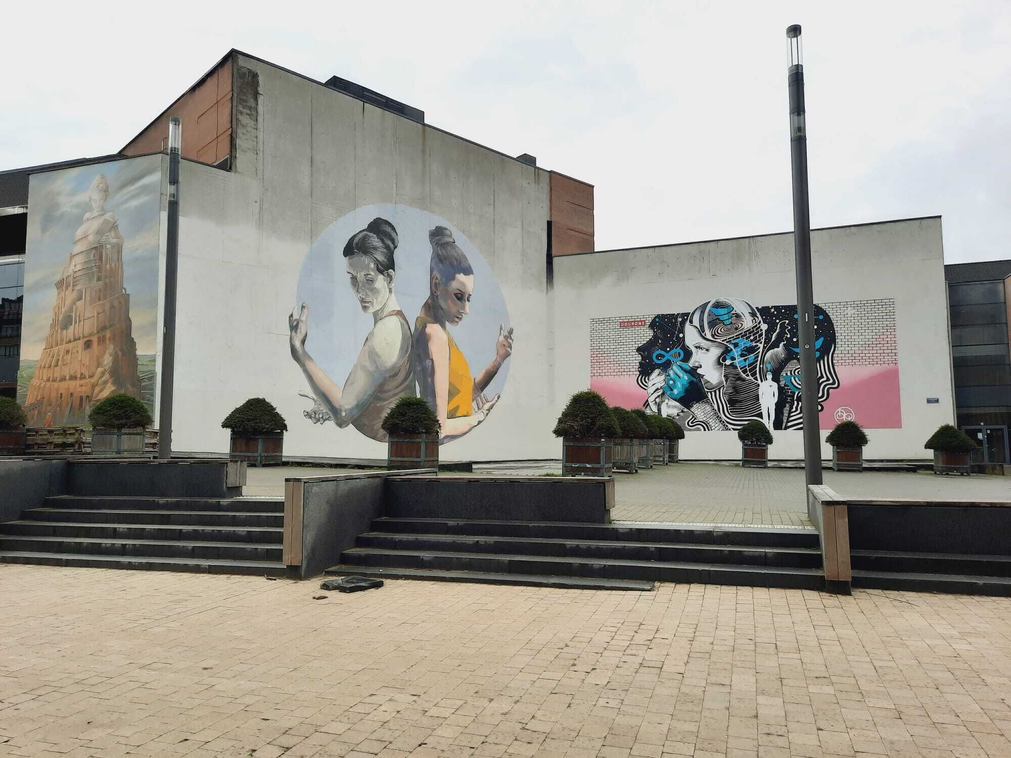 A building with a large mural on its side, featuring a mix of architectural and human figures.