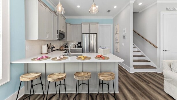 A modern kitchen with white cabinets, a central island with stools, stainless steel appliances, and pendant lighting. - Steps to beach, BBQ, bikes, pool, arcade, Wifi (Gulf Shores)