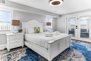 Une chambre avec un grand lit, des tables de chevet blanches, un tapis à motifs bleus et une vue sur l’extérieur par la porte.