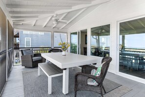 Une terrasse couverte avec une table blanche et des chaises en osier, de grandes portes-fenêtres coulissantes et une vue sur l’océan.