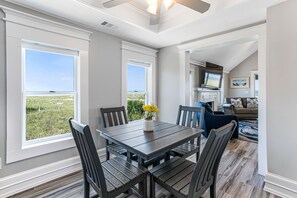 Un espace repas comprenant une table et des chaises, de grandes fenêtres, un ventilateur de plafond et une vue sur l’extérieur.