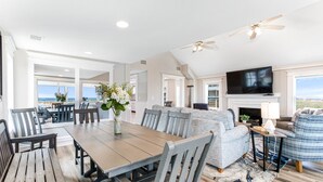 A spacious living area with a large wooden dining table, grey upholstered sofas, and a television mounted above a fireplace. - Our most Popular Rental on Tybee! Voted best view! by Tybee Cottages (Tybee Island)
