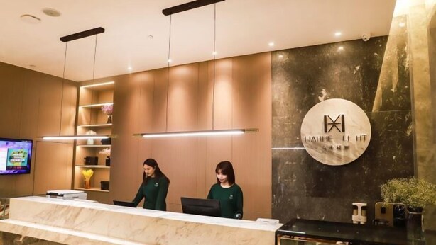 A modern reception desk with two staff members, a television, and a wall-mounted logo. - Wahme Light Hotel (Shangrao)