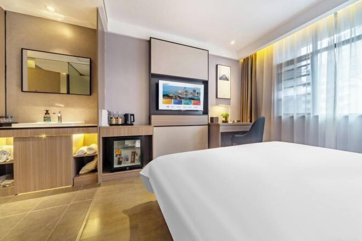 Une chambre d’hôtel équipée d’un lit, d’une télévision, d’un minibar, d’un bureau et d’une grande fenêtre avec des rideaux.