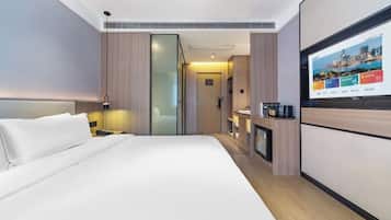 A modern hotel room with a large bed, a flat-screen TV mounted on the wall, and a small kitchenette area.