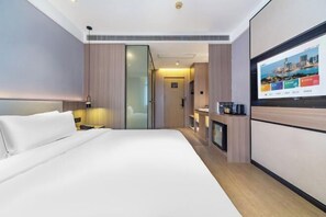 Una habitación de hotel moderna con una cama grande, un televisor de pantalla plana en la pared y una pequeña zona de kitchenette.
