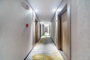 Pasillo de hotel con puertas a ambos lados, un detector de incendios en la pared izquierda y una alfombra estampada.