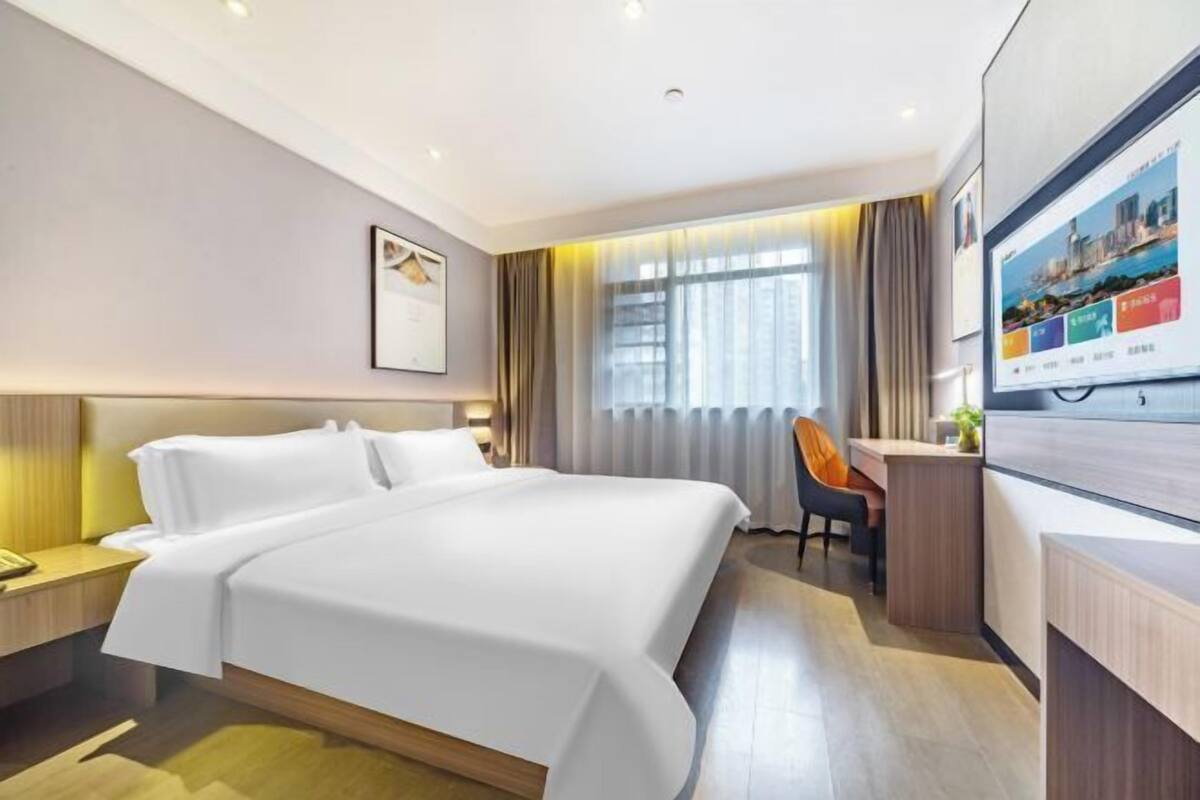 Une chambre d’hôtel avec un lit, un bureau, une chaise, une télévision et une fenêtre avec des rideaux.