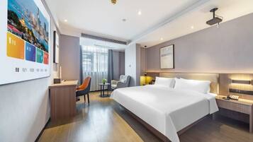 A modern hotel room with a large bed, a desk, a chair, and a small table.