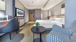 A modern hotel room with a bed, a desk, a chair, a small table with a plant, and a houndstooth sofa. - Wahme Light Hotel (Shangrao)