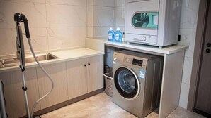 A compact laundry area with a washing machine, a dryer, and a hose. - Wahme Light Hotel (Shangrao)