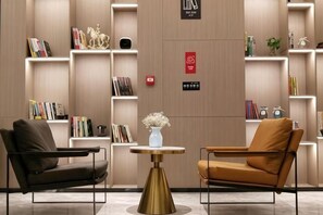 A modern lobby with two armchairs, a round table with a vase, and a bookshelf with books and decorative items. - Wahme Light Hotel (Shangrao)