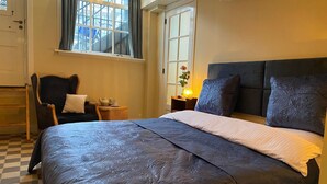 Ein Schlafzimmer mit einem großen Bett, einem Sessel, einem Nachttisch mit Lampe und einem Fenster mit Vorhängen.