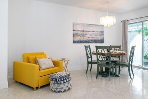 A bright yellow sofa with a matching ottoman, a wooden dining table with chairs, and a large abstract painting on the wall.