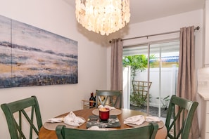 Uma área de refeições com mesa de madeira, cadeiras verdes, uma vela vermelha e um quadro na parede.