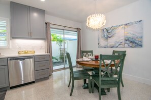 Une cuisine moderne avec des meubles gris, un lave-vaisselle et un coin repas comprenant une table ronde et des chaises vertes.